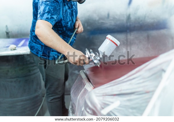 Auto mechanic\
painting a red car in a workshop.\
