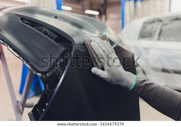 Auto mechanic preparing the car\
for paint job by applying polish with the power buffer\
machine