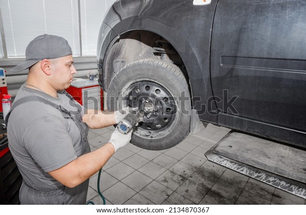 Auto Mechanic putting on a new tire. Mechanic\
changes the wheel on a modern car..Mechanician changing car wheel\
in auto repair shop.