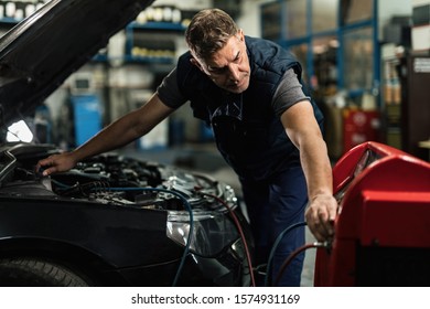 Auto Mechanic Recharging Air Conditioning Unit Of A Car In Repair Workshop. 