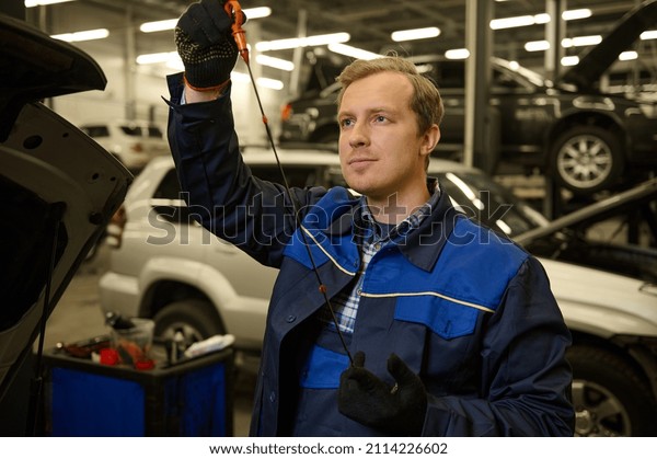 Auto mechanic repairer\
checking level of oil in car engine, under the hood, of the vehicle\
service shop
