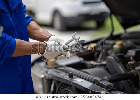 Auto mechanic repairing engine using wrench in garage. Mechanic in a jumpsuit fixes a car engine in a garage workshop.