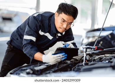 Auto mechanic repairman using a digital tablet to check the condition of engine room in the garage before changing spare parts, checking the mileage of the car, maintaining service automobile car  - Powered by Shutterstock