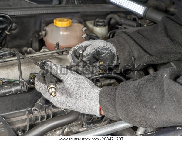 Auto mechanic replacing broken Diesel\
glow plug wire in car diesel engine\
compartment