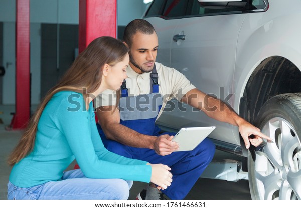 Auto\
Mechanic Showing to a Woman the Tire of her\
Car