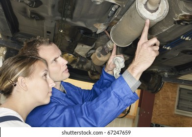 Auto mechanic shows the female trainee maintenance of the Car muffler under a car on a hoist - Powered by Shutterstock