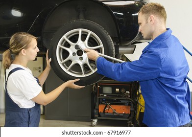 Auto mechanic shows the female trainee changing the wheels of a car in workshop in front of a car - Powered by Shutterstock