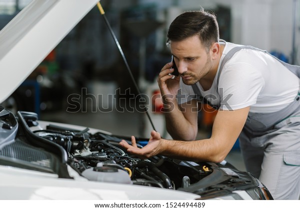 Auto\
mechanic talking on mobile phone in auto repair\
shop