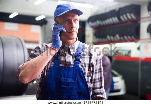 Auto mechanic talking on mobile phone with\
client in auto workshop
