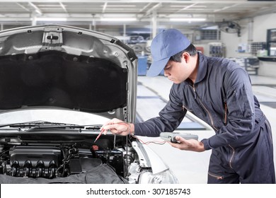 Auto Mechanic Uses A Voltmeter To Check The Voltage Level In A Car Battery At Repair Shop
