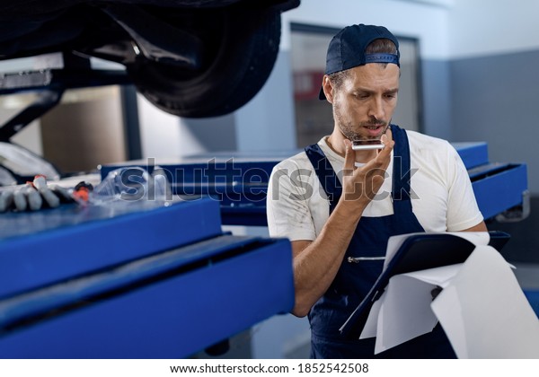 Auto mechanic using cell phone and talking\
on a speaker while working in repair shop.\
