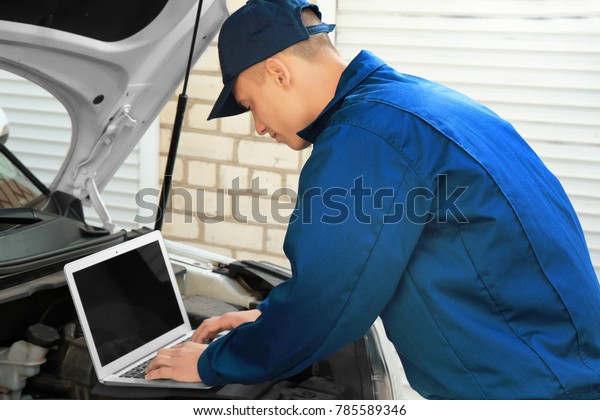 Auto mechanic using computer diagnostic program\
while repairing car\
outdoors