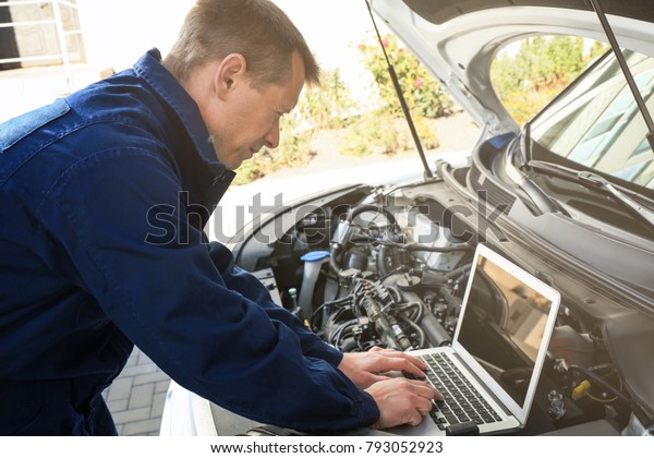 Auto mechanic using computer diagnostic program\
while repairing car\
outdoors