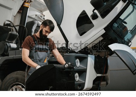 Auto mechanic using a diagnostic tool, carefully examining a truck engine in a garage workshop, focused on troubleshooting and repairs