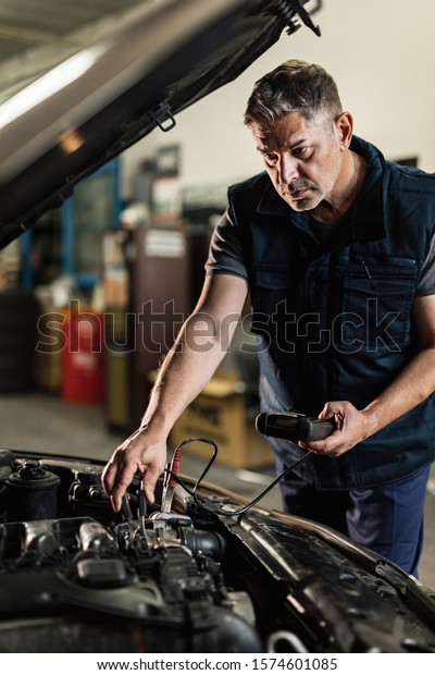Auto mechanic using diagnostic tool while\
checking car battery in repair workshop.\
