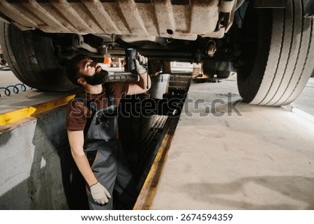 Auto mechanic using a flashlight, inspecting the underside of a truck in the service bay, ensuring thorough maintenance and repair