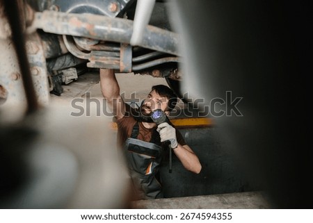 Auto mechanic using flashlight while inspecting the undercarriage of a truck in a repair garage