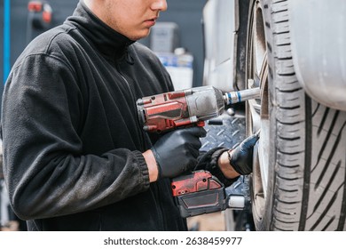 Auto mechanic using power tool to tighten car wheel bolts in garage workshop
