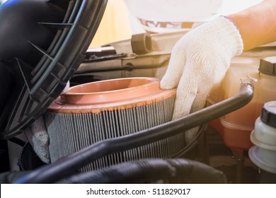 auto mechanic wearing protective work gloves holding a dirty, air filter over a car engine for cleaning