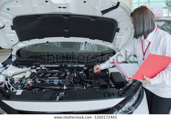  Auto mechanic Women (or technician) checking car\
engine at the garage. , record on red clipboard  at the repair shop\
Or service center