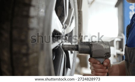 Auto mechanic worker changing a flat tire and alloy wheel using a professional air impact wrench tool in a garage