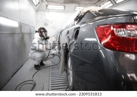 auto mechanic worker painting, automobile repairman painter in protective workwear and respirator painting car body in paint chamber