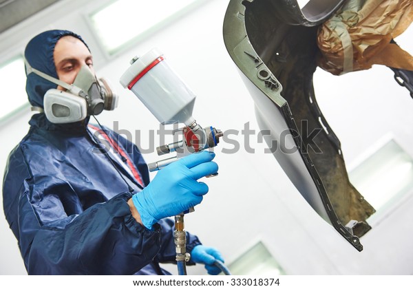 auto mechanic worker painting auto car bumper
in a paint chamber during repair
work