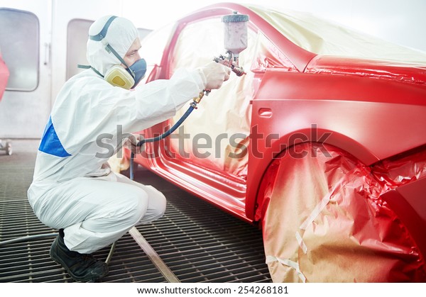auto mechanic worker painting a red car in a paint\
chamber during repair work