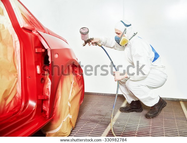 auto mechanic worker painting a red car in a paint\
chamber during repair work