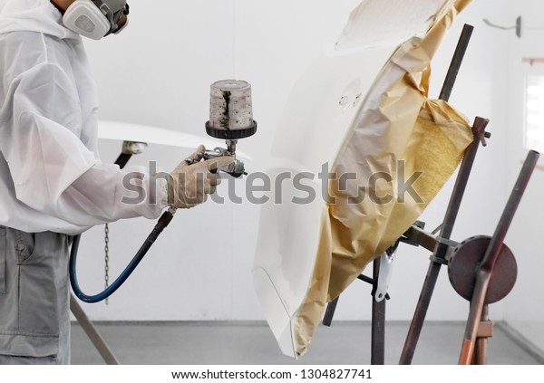 Auto mechanic worker painting a white car in\
a paint chamber during repair\
work