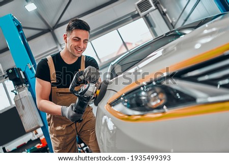 Auto mechanic worker polishing car at automobile repair and renew service station shop by power buffer machine. Selective focus. Close up view.