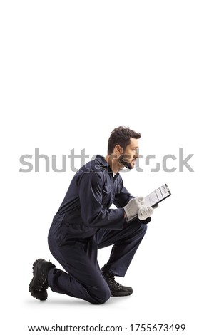 Auto mechanic worker in a uniform kneeling and writing a document isolated on white background