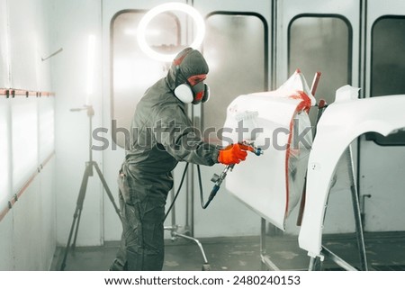 Auto mechanic worker wearing protective workwear spraying white paint on car part at workshop