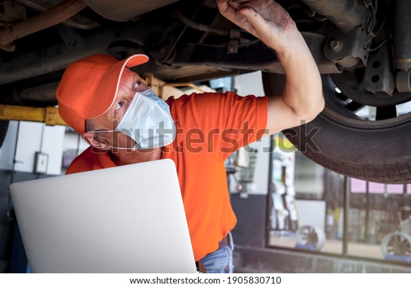 Auto mechanic working in garage, car service\
technician checking and repairing the customer car at automobile\
service center, inspecting car under body and suspension system,\
vehicle repair shop.