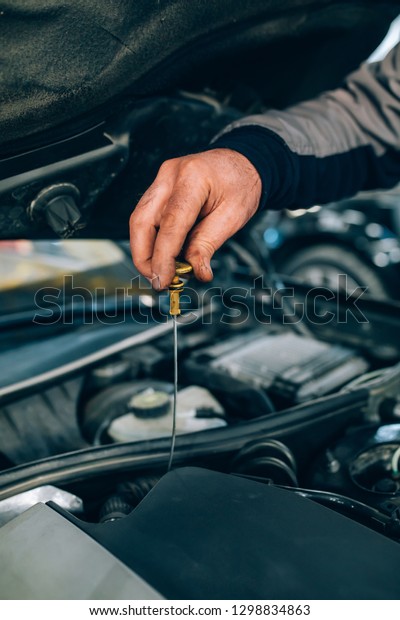 Auto mechanic working in garage during the\
maintenance of engine. Mechanician pushing dipstick during Repair\
of a car in auto service\
garage