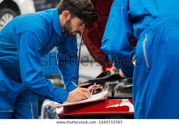 Auto mechanic working in\
garage.Vehicle service maintenance young handsome men check car\
condition in garage. Auto Service Center, repair, maintenance\
concept 
