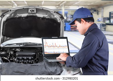 Auto Mechanic Working On A Computer Connected To A Car Engine At Repair Shop