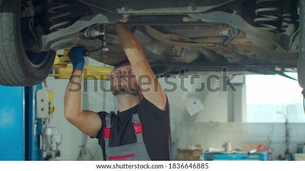 Auto mechanic working\
underneath car lifting machine at the garage. Auto repair shop, Car\
service, repair.