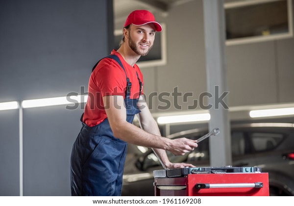 Auto mechanic\
with wrench in hand near\
toolbox
