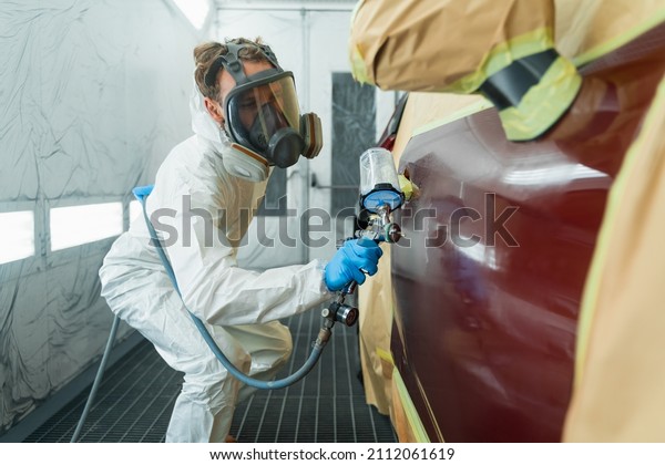 Auto painter in a\
protective suit and mask sprays a degreaser or other cleaner on a\
car door using a spray gun. Preparation of vehicle body elements\
for local repair