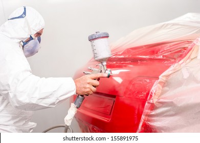 Auto painter spraying red paint on car in auto workshop