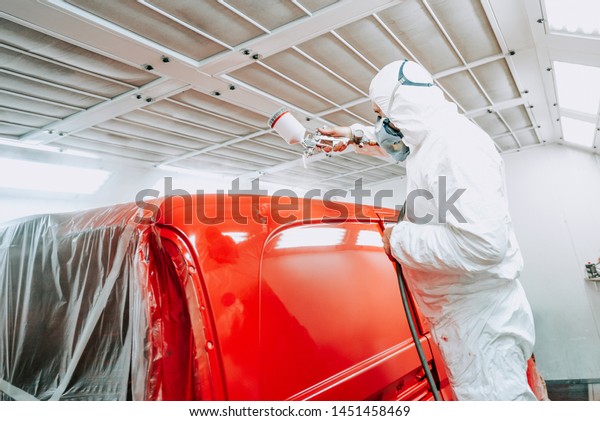 Auto painter spraying red paint on van, car in\
auto workshop