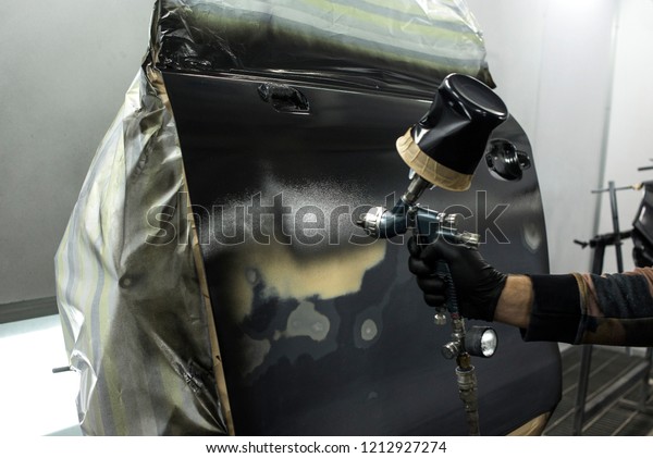 Auto painter spraying white paint on car detail  in\
special booth