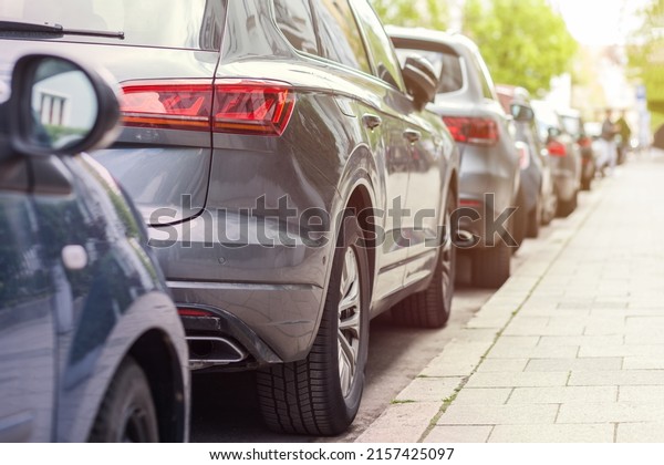 Auto parking\
problem. Long row of different Cars parked along empty roadside on\
blurred green foliage bokeh background. Modern city lifestyle,\
vehicles parking problem\
concept.