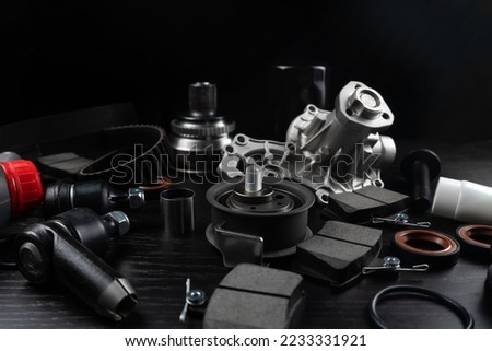 Lot of auto parts lie on wooden black background. Engine and suspension parts, swivel knuckle, joint and engine parts unfolded. New spare parts. Bearings . Play by light. Hanging on table.