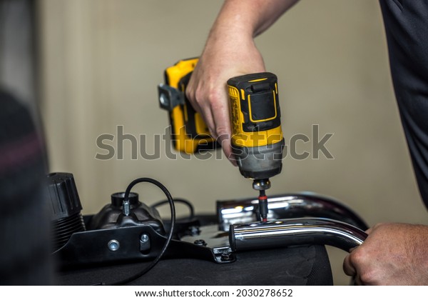 An auto repair man using a drill and fixing\
a car part in an auto repair\
shop.