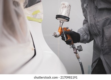 auto repair painter in protective workwear and respiratory painting car body in paint chamber