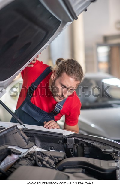 Auto, repair. Serious looking man\
under the open hood of car being repaired in\
garage