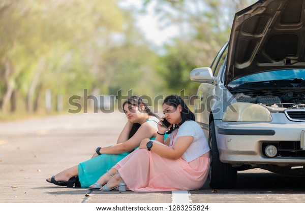 Auto\
repair service, Insurance Concept - Teen driver using smartphone\
after car accident. Asian woman worry and stress a trouble with car\
engine crash overheat at the side of the\
road.