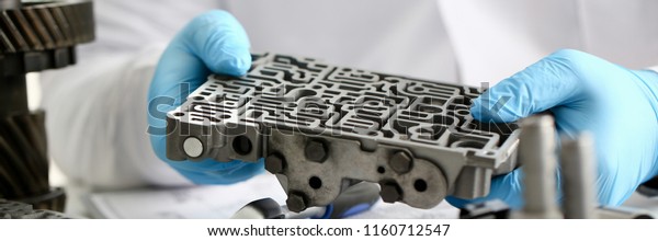 The auto repair service repairman in automatic\
gearboxes holds in his hand in blue protective gloves the\
hydroblock detail dehydrates the diagnostics and estimates detail\
test transmission closeup.